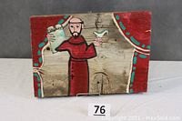 Full view of the Saint Francis painting on wood board with red curtain background, dove in left hand, tablet in right hand.