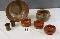 Photo of all pottery items including large bowl, 3 smaller matching bowls, hanging bowl, and 2 juice glasses arranged on white cloth.