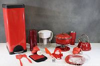 Wide view showing all included red kitchen items arranged side by side on a gray surface with gray backdrop
