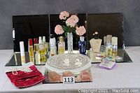 Six 12-inch beveled square mirrors arranged behind an assortment of perfume bottles, glass tray, red velvet pouch, and vase with pink flowers.