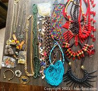 Top view of assorted colorful bead necklaces, gold chains, and costume jewelry pieces laid out on a wooden surface.
