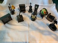 Ten differently shaped vintage pencil sharpeners resembling antique household items spread on a white cloth.