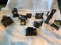 Photo of 10 vintage miniature pencil sharpeners arranged on white cloth, showing various antique household appliance shapes.