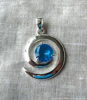 Front view of sterling silver spiral pendant with aqua blue stone set in center.