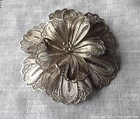 Front detail of the silver filigree flower brooch showing layered petals and intricate wirework patterns.