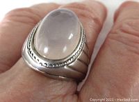 Close-up of the ring on a finger showing the oval moonstone cabochon and silver band with decorative beaded edge.
