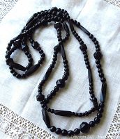 Full view of the long black Whitby jet bead necklace laid on white fabric, showing various bead shapes and sizes.