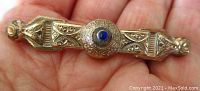 Front view of Victorian gold plated bar brooch showing detailed design and blue center stone on a hand for scale.