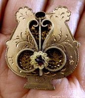 Front view of Victorian gold plated brooch showing engraved scroll design and red center stone