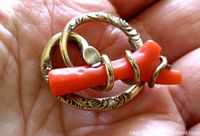 Close-up of brooch showing coral branch wrapped in gold wire and engraved circular frame.
