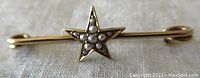 Close-up of the star-shaped gold brooch adorned with seed pearls, showing front details and pearl arrangement.