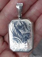 Photo of front side of the rectangular locket showing floral engraved design and bail detail.