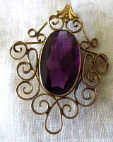 Close-up front view of antique gold wash brass pendant with large faceted oval purple amethyst paste stone and ornate scrollwork filigree