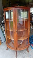 Full view of cabinet showing bow front curved glass double doors and side panels, oak frame with brass handles and curved legs.
