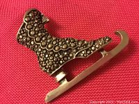 Front side view of silver-tone ice skate brooch showing decorative textured pattern and smooth blade.