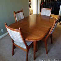 Front-angle view of teak table top and four chairs showing wood grain and finish