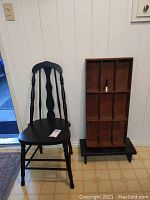 Overall view of black chair beside wooden cubby shelf on black stand against wall