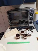 Hamilton Beach stainless steel countertop oven alongside ten ceramic salt dishes and three set knife sharpeners with knives.