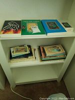 Top shelf of white bookshelf showing four main books, tarot card deck, and amethyst stone.