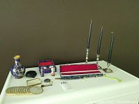 Full lot display showing cloisonné items including lighter holders, makeup brush, blade with sheath; brass vase on wooden stand; brass coaster; three brass candlesticks with black candles