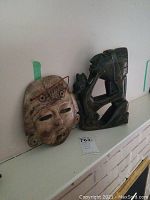 View of both stone statue and wooden mask together on a shelf.