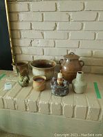 Full view of all items including the large ginger jar, metal bird, candle holder, and smaller pottery pieces arranged on a beige brick surface
