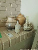Four pottery pieces displayed on brick shelf including large crackle pattern vase, tall urn vase, lidded round pot, and small beige vase with gold accents.