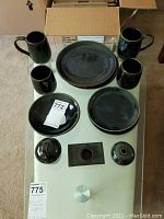 Wide view of entire stoneware set for two including mugs, cups, plates, and bowls in dark blue glaze.