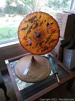 Full view of the hand painted parasol, woven rattan hat, and green parasol on glass table near window.