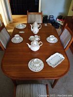 Overview of full china set arranged on table including tea pot, coffee pot, sugar bowl, creamer, plates, cups and saucers