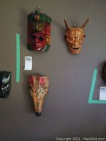 Three hand-carved wood masks mounted on wall showing the colorful Aztec-style mask, tan dog mask, and tan Oni demon mask.