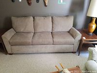 Front view of beige three-cushion sofa against wall