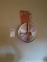 Wall-mounted gong with wooden backboard and hanging mallet shown in full.