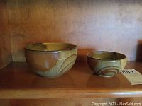 Photo of two matching pottery bowls on wooden shelf, larger bowl on left, smaller on right