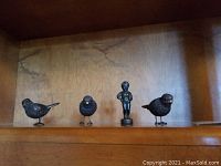 Four figurines displayed on a wooden shelf including three birds and one boy figurine.