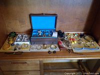 Photo showing assortment of costume jewelry including bangles, necklaces, earrings, and the wooden jewelry box with blue lining on wooden surface.