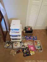 Overview photo showing diverse crafting supplies including multiple plastic storage containers, paint tubes, craft materials, and unopened glue guns.