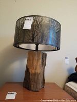 Full front view of the lamp showing composite tree stump-like base and black metal tree-branch pattern lampshade.