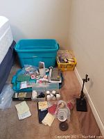 Full lot view showing large blue plastic tub and a yellow basket with many fishing lure making supplies spread on carpeted floor next to bed.