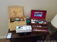 Photo of two sewing boxes on a wooden table with various sewing supplies visible including spools of thread, buttons, and measuring tape