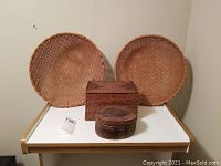 Full view of two round woven baskets and two woven lidded boxes on a table.