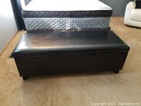Full view of black cushioned storage bench closed, showing rectangular shape and short legs.