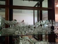 Shelf displaying various clear crystal and glassware including stemware, small dishes, shakers with silver caps, ashtray, and decanter stopper.