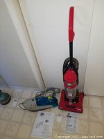 Red Dirt Devil upright vacuum, blue and gray Dirt Devil Spot Scrubber, and two instruction manuals on a tiled floor.