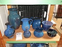 Collection of blue pottery dishes including jugs, bowls, and a small vase, displayed on a wooden shelf.