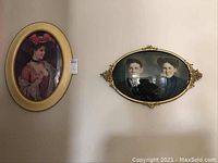 Two antique portraits hanging on wall, one oval hand-colored portrait of a man and woman in gold ornate metal frame, one oval print portrait of a woman in pink dress and hat in gold domed glass frame.