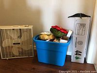 Photo showing a white Galaxy box fan, a blue plastic tub filled with Christmas decorations including poinsettia wreath and ornaments, and a boxed 4-foot pre-lit Christmas tree.