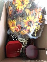 Box with various small doll furniture pieces and a plastic-wrapped fall wreath containing sunflowers, pine cones, and feathers.