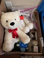 Box containing multiple plush polar bears and some ceramic figurines, largest plush bear with a red ribbon bow.
