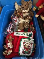 Plastic tub filled with multiple plush and ceramic Christmas bears, assorted sizes and designs visible, along with holiday stockings and ornaments.